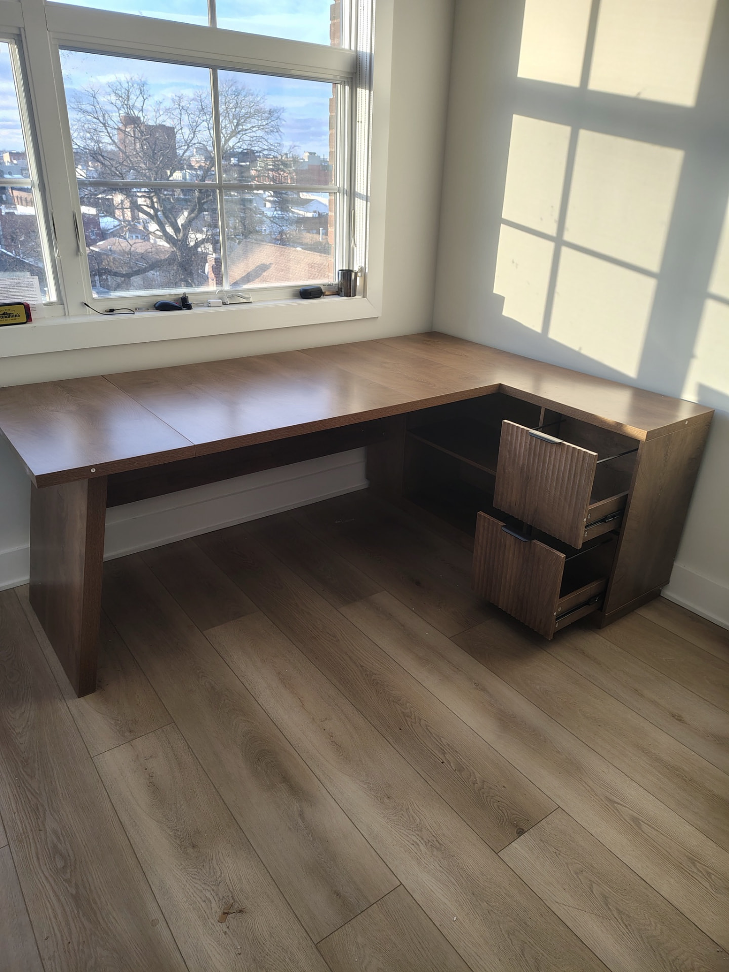 Wood corner desk below a bright window.